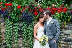groom kisses bride on the forehead in front of a wall of flowers at Fernhill House Hotel