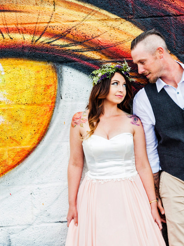 Bride and Groom look at each other in front of a mural of a giant yellow eye. 